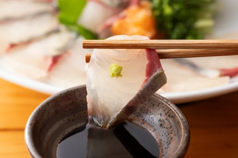 わさびを添えた刺身を醤油で味わう